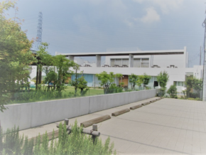 Modern white two‑story building with a green lawn, trees, and a paved parking area with wheel stops in the foreground.