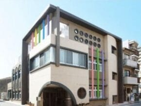 Modern beige building with a large rounded entrance and vertical colorful panels on the facade.