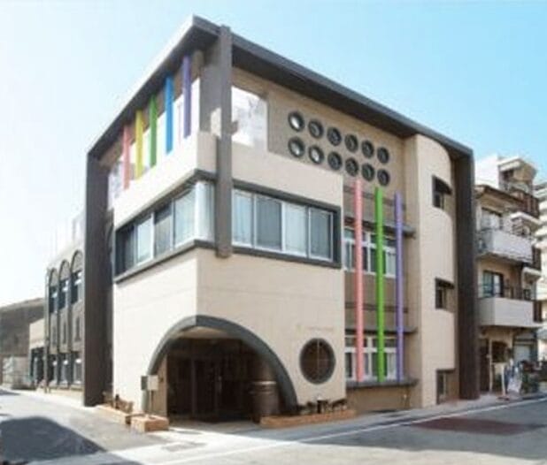 Modern beige building with a large rounded entrance and vertical colorful panels on the facade.