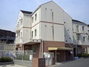 Three-story beige apartment building with a brick base and gated entrance in a residential complex
