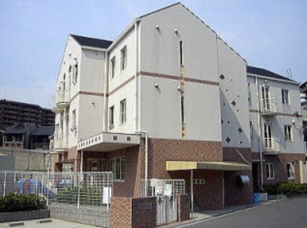 Three-story beige apartment building with a brick base and gated entrance in a residential complex