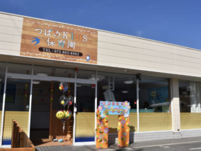 Front entrance of a Japanese daycare『つばめKIDS 保育園』with colorful balloons and a decorative flower arch; sign displays phone number 072-803-8963.