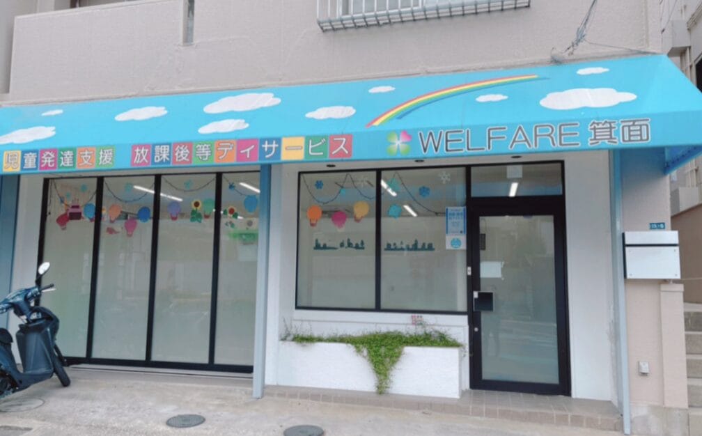 Storefront with a bright blue awning reading 'WELFARE' and Japanese text, large windows, and a scooter parked outside.