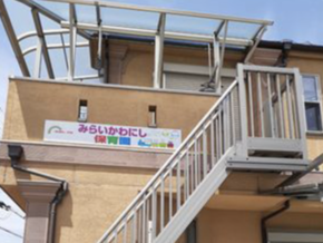 Two-story beige building with a metal outdoor staircase and a colorful sign in Japanese on the wall.