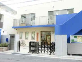 Front entrance of a white building with a bright blue extension and a folding gate, likely a small clinic or community facility.