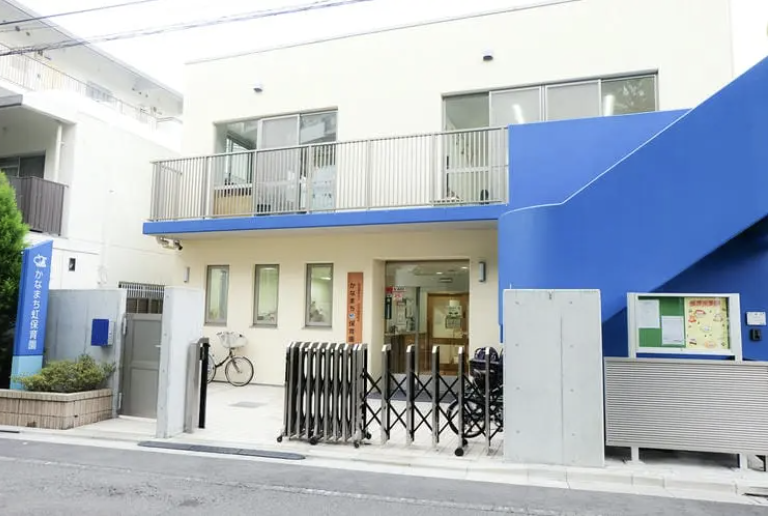 スクリーンショット 2026-09-11 160747 | 保育士求人|大阪・兵庫・関西の保育士・幼稚園教諭の就職転職支援|保育のせかい Front entrance of a white building with a bright blue extension and a folding gate, likely a small clinic or community facility.