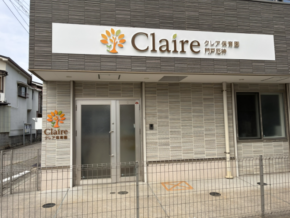 Front entrance of a daycare or preschool named 'Claire' with an orange tree logo on a white sign, frosted glass doors, beige brick facade, and a small metal fence.