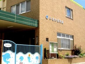 Exterior of Izumi Hoikuen preschool: brick building with a green canopy, blue decorative gate, and a small garden.