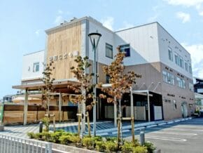 Modern two-story building with wooden panels and light-colored exterior, signage on the front, with a small landscaped area and parking lot. (informative)