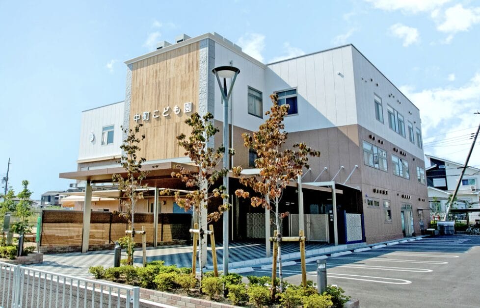 Modern two-story building with wooden panels and light-colored exterior, signage on the front, with a small landscaped area and parking lot. (informative)