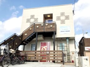 Modern two‑story building with an external wooden staircase, decorative wall panels, and bikes parked along a wooden fence in front.