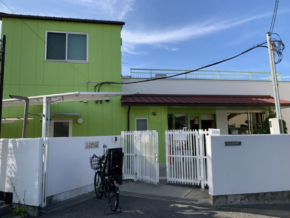 Two-story lime-green building with a white gate and a parked bicycle in front against a blue sky.