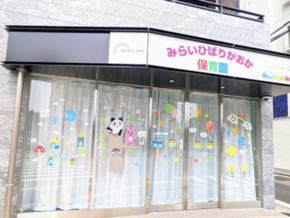 Colorful kindergarten storefront with large glass doors and playful window decorations for children (train, houses, animals).