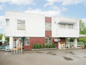 Two-story white-and-brick building with plants along the front and a small playground on the left on a wet paved area.