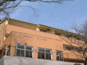Two-story orange-brick school or community building with large windows and outdoor walkway, under a clear blue sky.