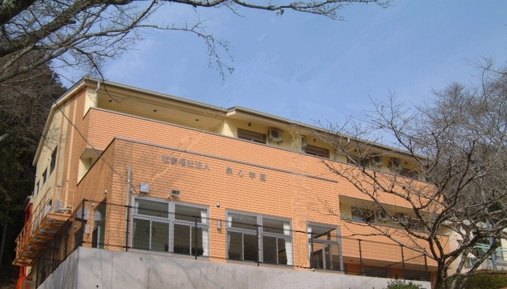 Two-story orange-brick school or community building with large windows and outdoor walkway, under a clear blue sky.