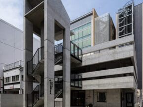 Brutalist concrete stairwell and parking structure in front of a modern glass building.