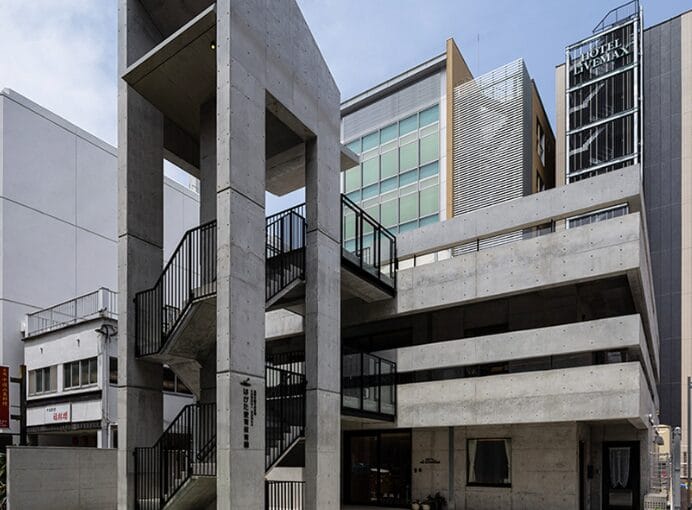 Brutalist concrete stairwell and parking structure in front of a modern glass building.