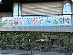 Colorful banner on a building with cartoon children, an open book, and the Japanese phrase '遊びと学びの森' (Play and Learn Forest).