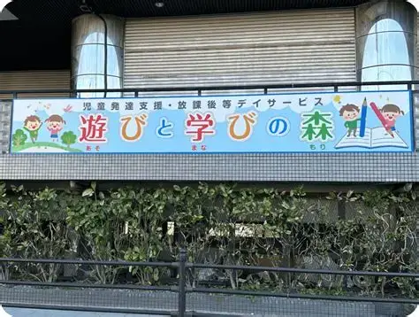 Colorful banner on a building with cartoon children, an open book, and the Japanese phrase '遊びと学びの森' (Play and Learn Forest).