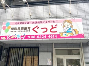 Exterior storefront sign for a children's developmental support and after-school service, with a large red 'ぐっど' and phone number 06-6224-4614, plus cartoon illustrations.