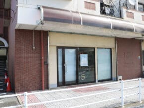 Closed storefront with glass doors and a poster in the window, on a brick building with a curved awning above.