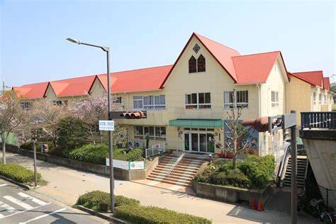 Beige, two-story building with red gabled roofs and a green awning over the main entrance, surrounded by trees and a sidewalked street in front.