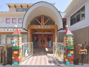 Kindergarten entrance with an arched roof, colorful castle towers, and double doors, inviting kids inside.