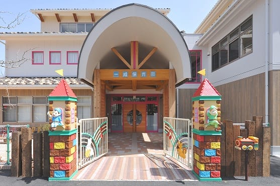 Kindergarten entrance with an arched roof, colorful castle towers, and double doors, inviting kids inside.