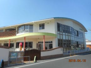 Two-story public building with a curved glass facade, green awning, and red columns along a sunny street. Date stamp 2018.04.13.