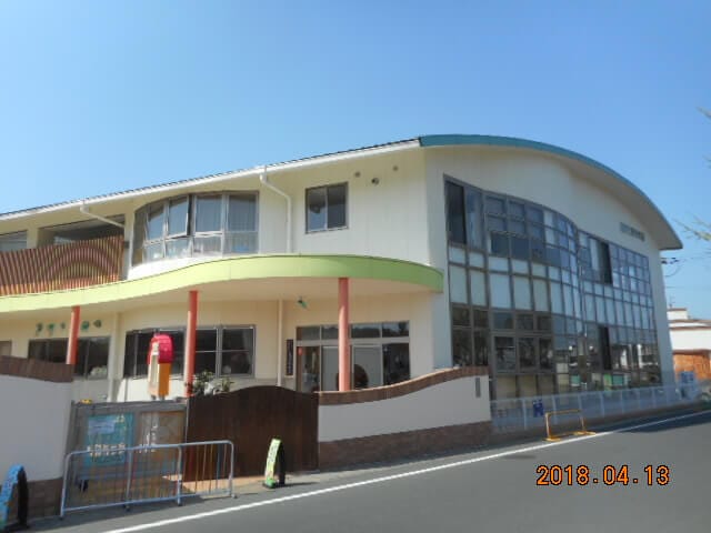 Two-story public building with a curved glass facade, green awning, and red columns along a sunny street. Date stamp 2018.04.13.