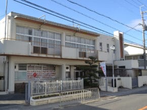 image | 保育士求人|大阪・兵庫・関西の保育士・幼稚園教諭の就職転職支援|保育のせかい White two-story building with large windows and an orange railing along a balcony, on a street with overhead power lines and a clear blue sky.