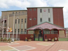 Colorful school building with a pink arched entrance and a brick courtyard foreground.