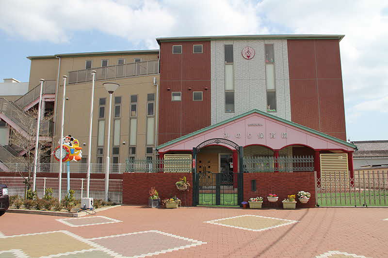 Colorful school building with a pink arched entrance and a brick courtyard foreground.
