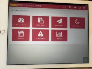 タブレット画面の赤いダッシュボードアイコン群。ダッシュボード、家庭から園へ、園から家庭へ、ブレスチェック、指導計画、共有情報管理、成長記録の各アイコンが並ぶ。