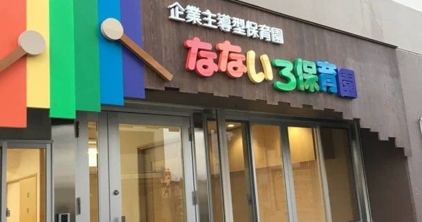 Colorful daycare center storefront with rainbow panels and Japanese signage above glass doors.