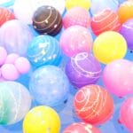 Assorted bright plastic balls with swirl patterns floating in a blue ball pit/pool.