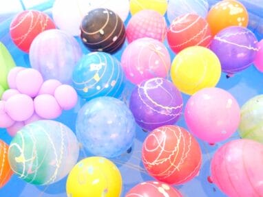 Assorted bright plastic balls with swirl patterns floating in a blue ball pit/pool.