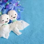 Two smiling tissue-paper dolls with pink cheeks sit among blue hydrangea flowers on a blue background.