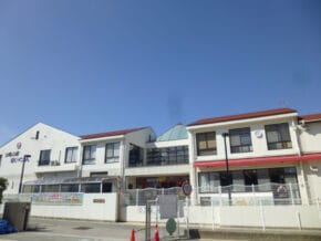 Front view of a white, two-story school building with a red roof and glass atrium under a clear blue sky.