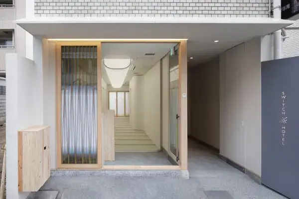 kyoto | 保育士求人|大阪・兵庫・関西の保育士・幼稚園教諭の就職転職支援|保育のせかい Modern hotel entrance with a wooden-framed glass doorway opening to a bright white interior hallway and stairs; exterior gray wall with the hotel name on the right.
