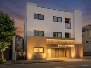 Modern white, three-story building at dusk with warm entrance lights; Japanese daycare sign above the entryway