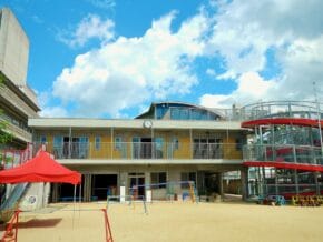Outdoor playground in front of a two-story yellow building with a red canopy and blue sky above.