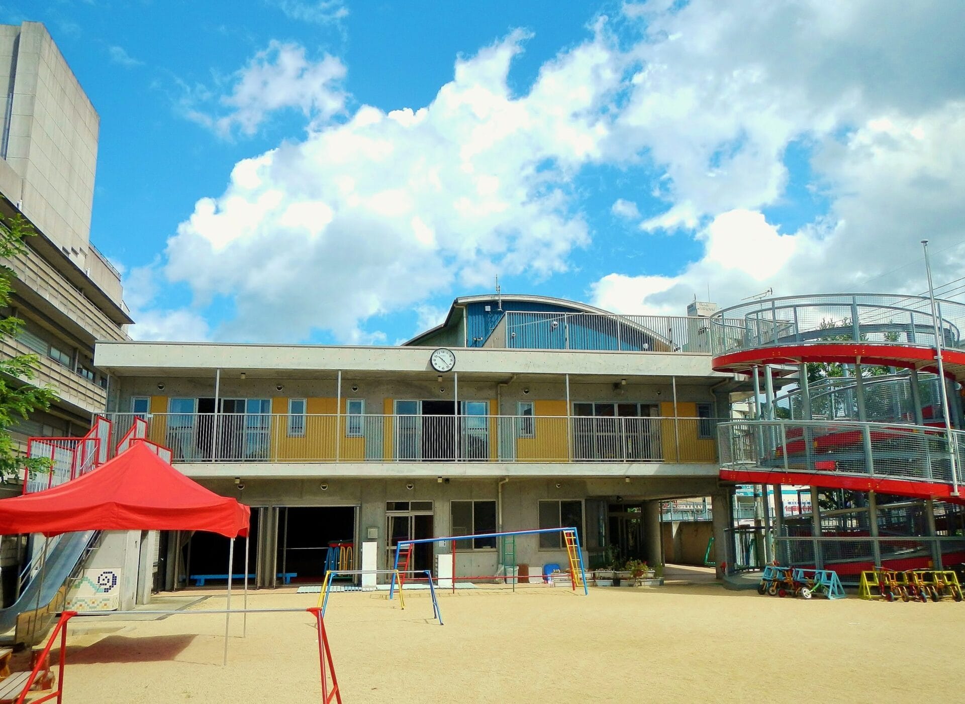 Outdoor playground in front of a two-story yellow building with a red canopy and blue sky above.