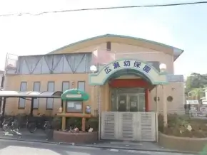 A small preschool building with a curved blue roof and a welcoming entrance arch; bicycles parked to the left and a small garden bed in front.