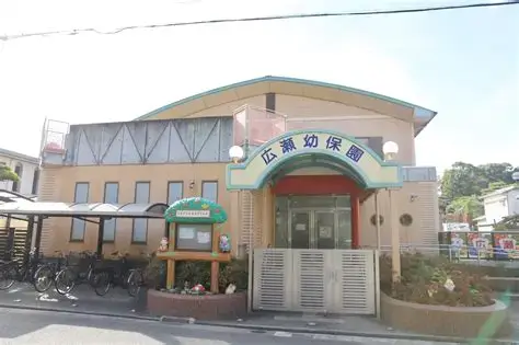 A small preschool building with a curved blue roof and a welcoming entrance arch; bicycles parked to the left and a small garden bed in front.