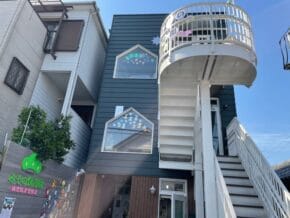 Two-story children's daycare building with a white external staircase, blue-gray siding, and windows decorated with colorful stickers.