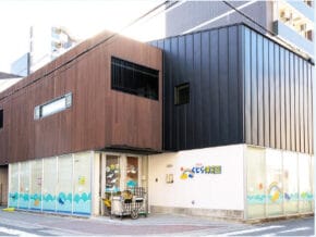 Two-tone modern building with brown and dark metal siding, glass storefronts with a blue wave pattern at the base, a cart parked near the entrance.