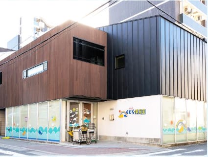 Two-tone modern building with brown and dark metal siding, glass storefronts with a blue wave pattern at the base, a cart parked near the entrance.