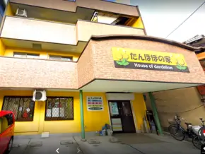 main_parts_0002341465_13 | 保育士求人|大阪・兵庫・関西の保育士・幼稚園教諭の就職転職支援|保育のせかい Three-story building with yellow trim and a sign reading 'House of dandelion', entrance under green columns with bicycles parked outside.